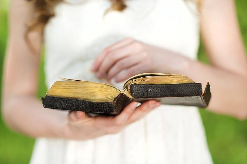 Otwarta Biblia w dłoniach dziewczynki w białej sukience