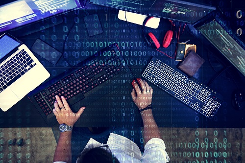 mężczyzna przy sprzęcie elektronicznym, laptopie, trzech ekranach i klawiaturze