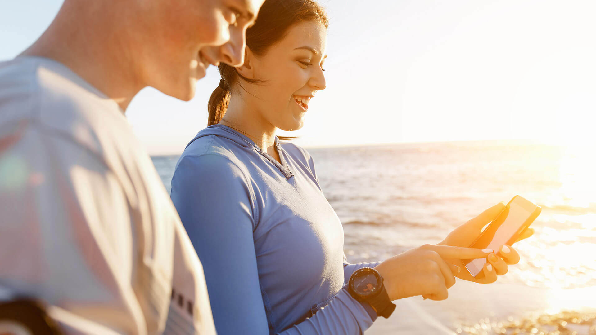 Kobieta i mężczyzna spacerujący po plaży i patrzący w telefon komórkowy