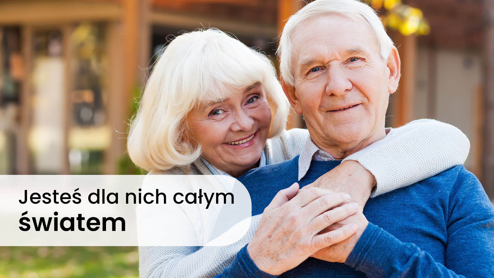 Starsza kobieta o siwych włosach przytulająca starszego mężczyznę ubranego w niebieski sweter