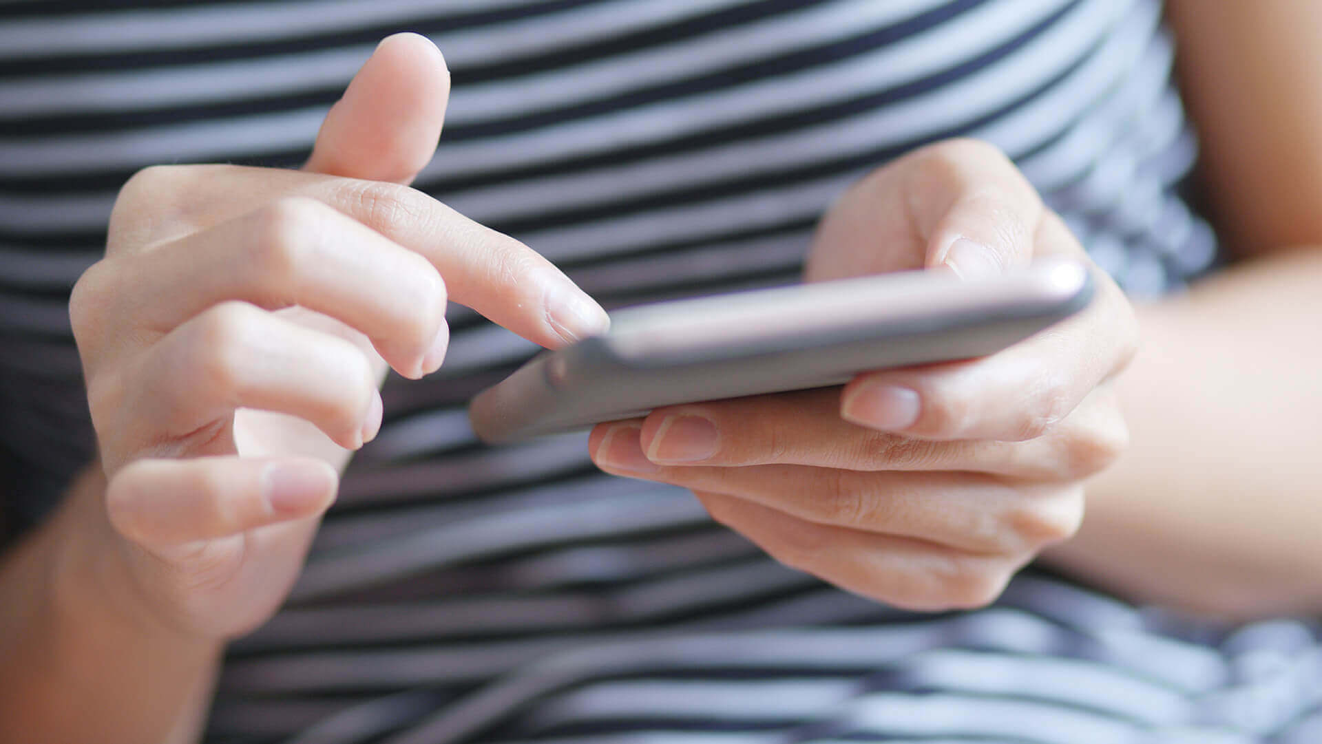 Telefon komórkowy trzymany przez kobietę ubraną w bluzkę w paski
