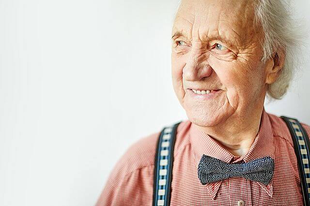 Starszy, uśmiechnięty mężczyzna z siwymi włosami, z elegancką muszką na szyi