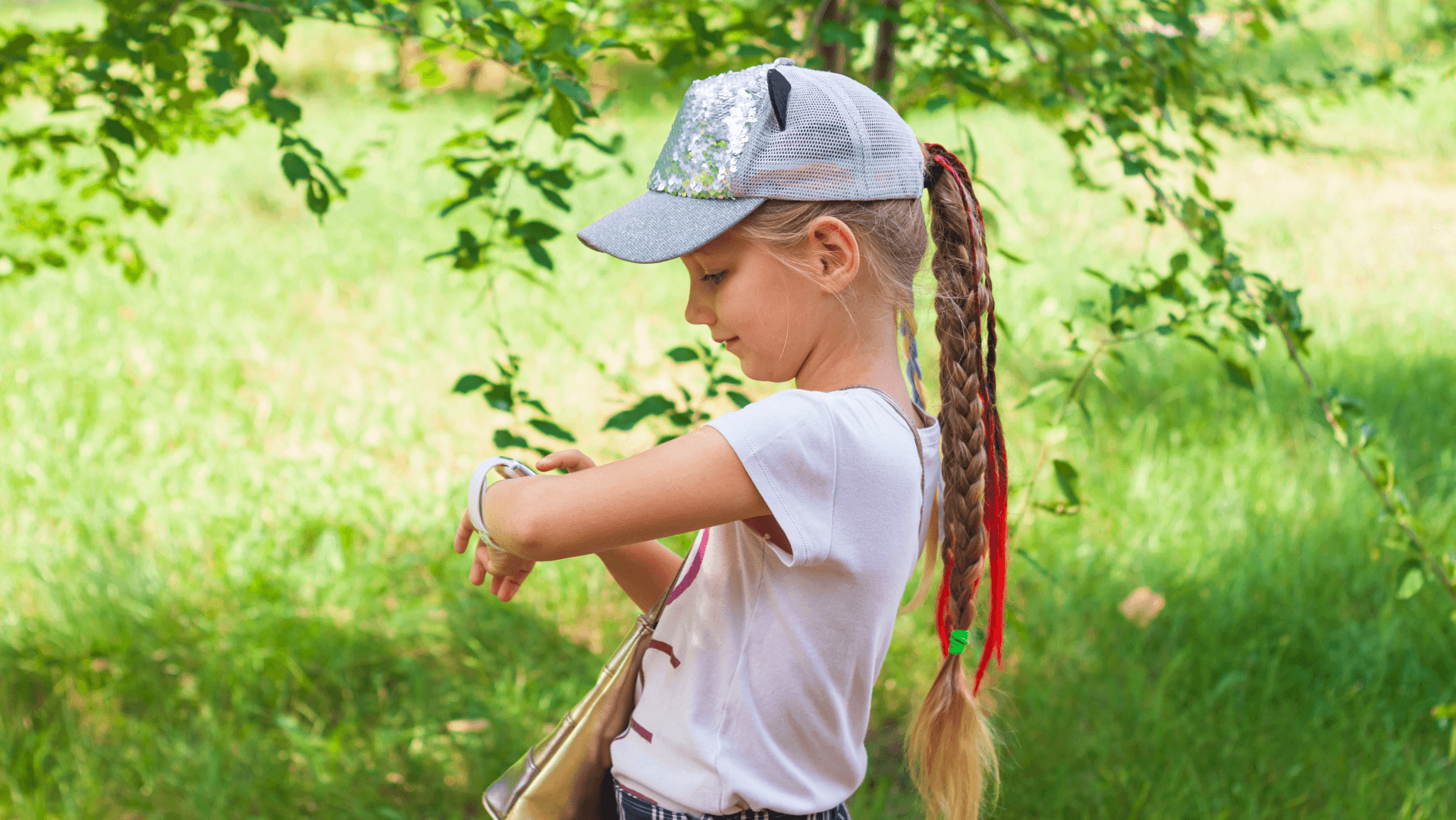 Kilkuletnia dziewczynka z czapką z daszkiem na głowie, patrząca na swój smartwatch GPS